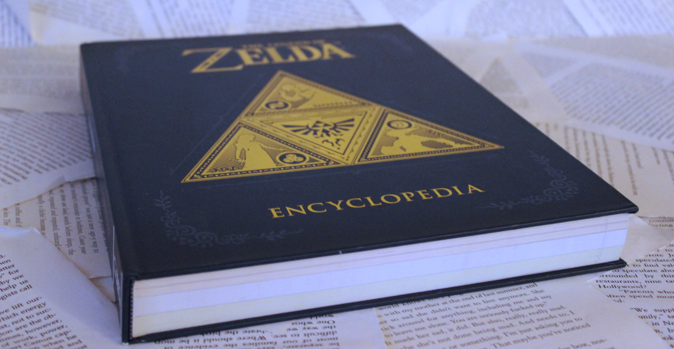 A photo of The Legend of Zelda Encyclopedia, a large blue hardcover book with a golden triforce on the cover.