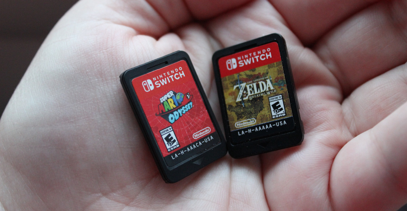 A hand holding two video game cartridges for Super Mario Odyssey and The Legend of Zelda: Breath of the Wild