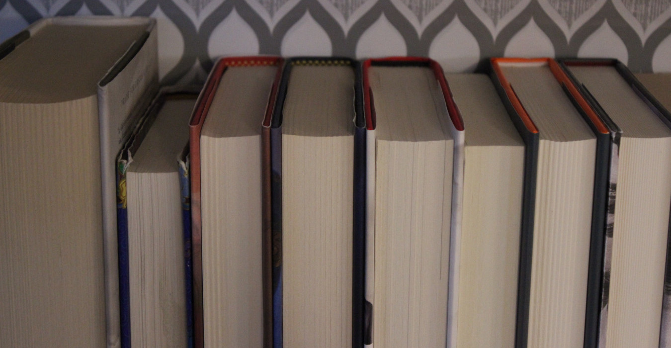 A collection of books on a shelf, but they're turned backwards so the pages face out instead of the spines.