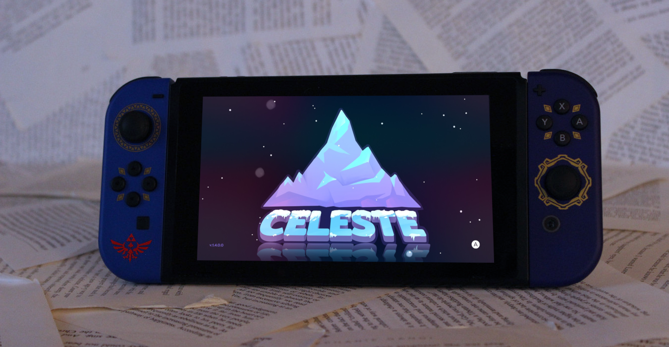 A Nintendo Switch console propped up against a paper background. The screen displays the game Celeste, with an illustration of a mountain