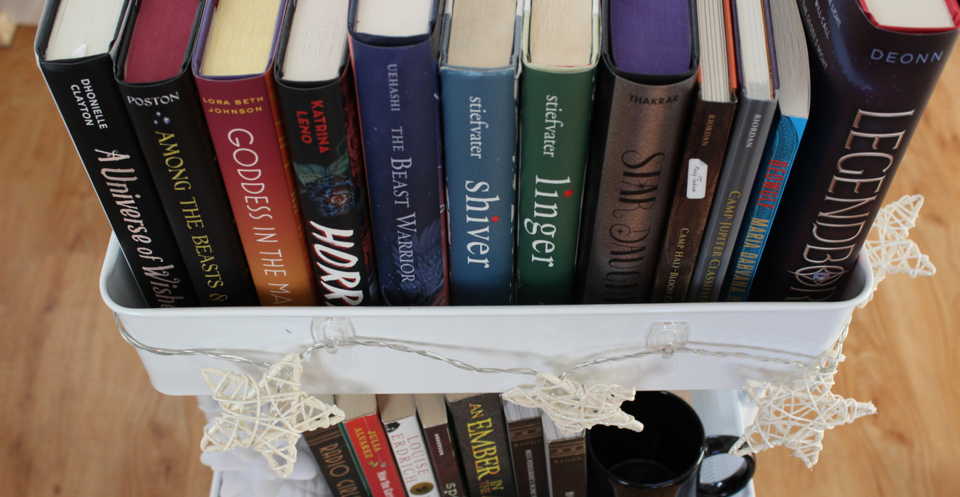 Several books sitting in a white metal cart. The cart is decorated with string lights shaped like stars.