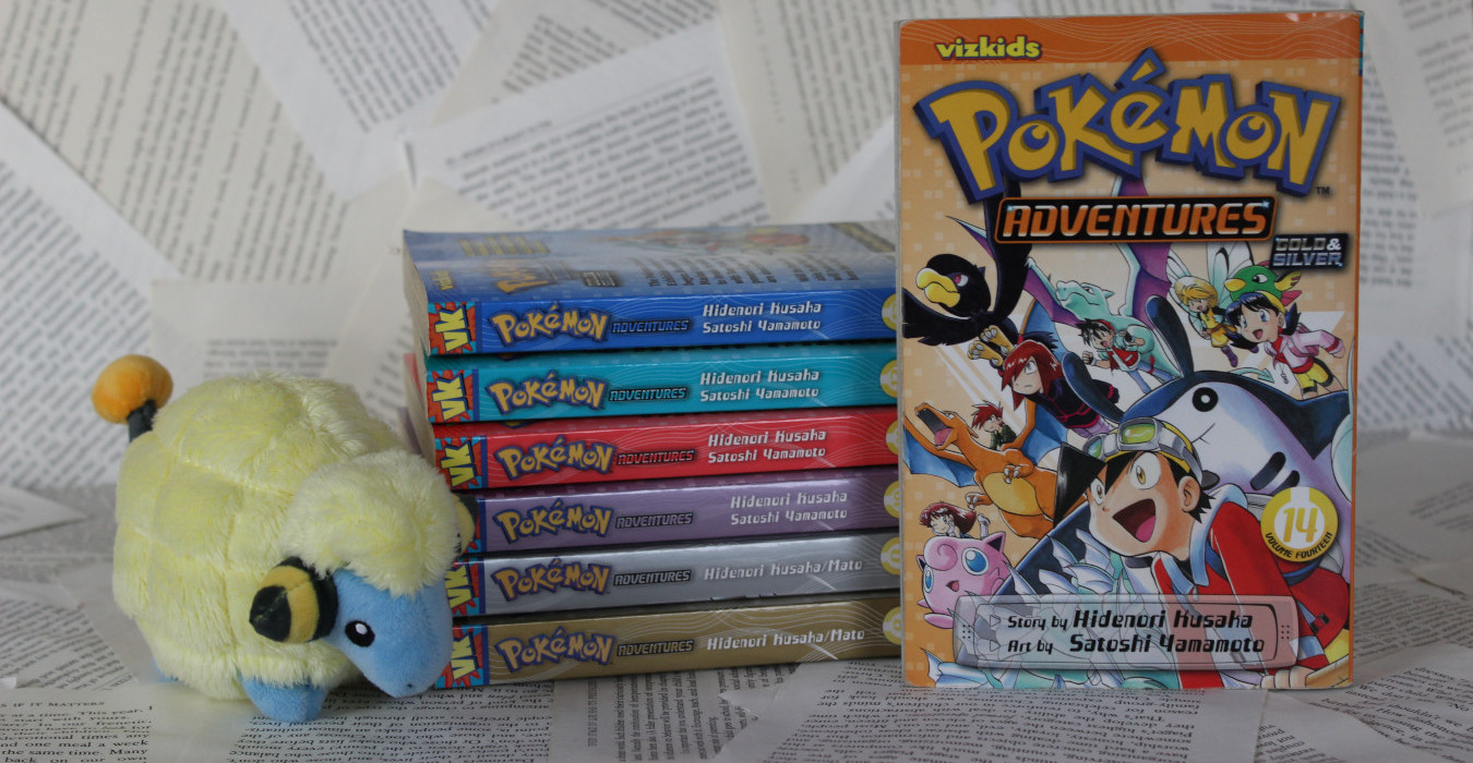 A stack of Pokemon Adventures manga volumes. Volume 14 is shown so the reader can see the cover. A small plush Mareep is next to the stack.