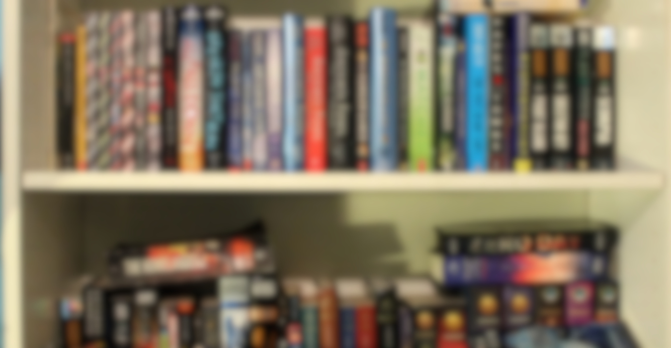 A blurred photo of many books on a bookshelf. None of the titles are readable, but there are a lot ofthem.