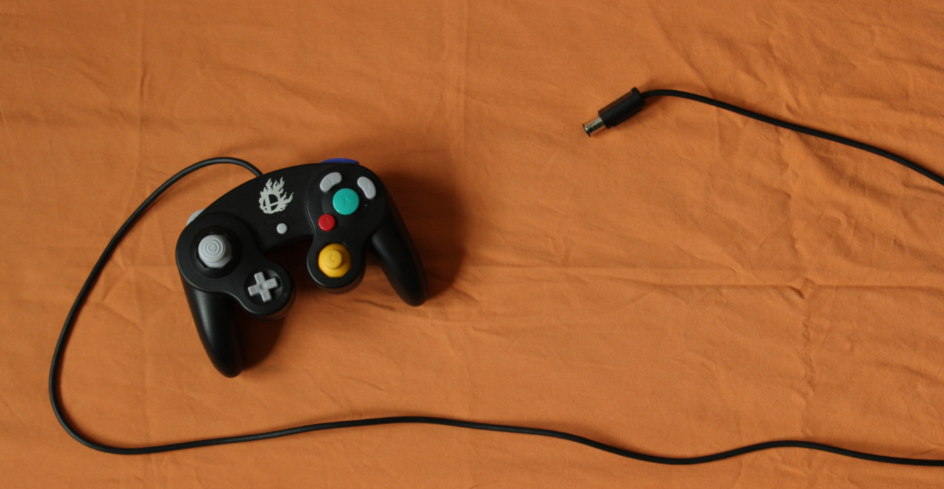 A GameCube video game controller sits against a plain orange background.