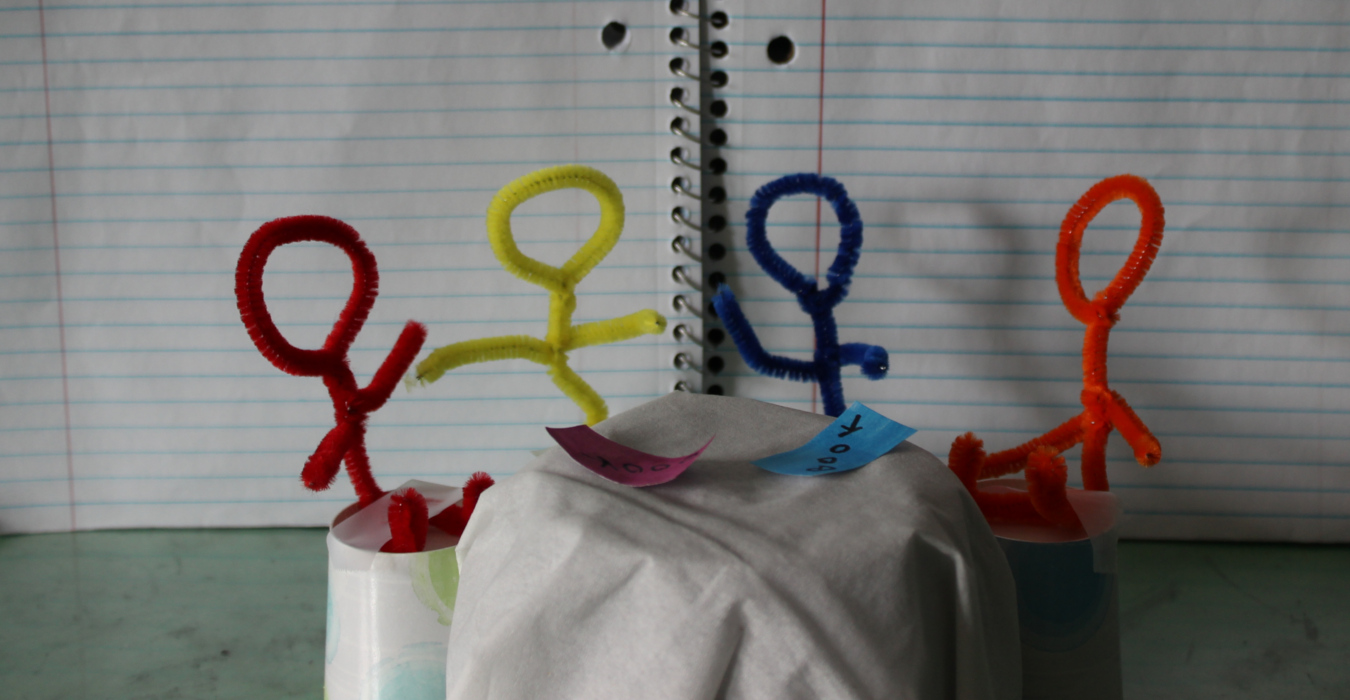 Several stick figures made of pipe cleaners sit around a "table". If they had faces, they would appear to be in a deep literary discussion.