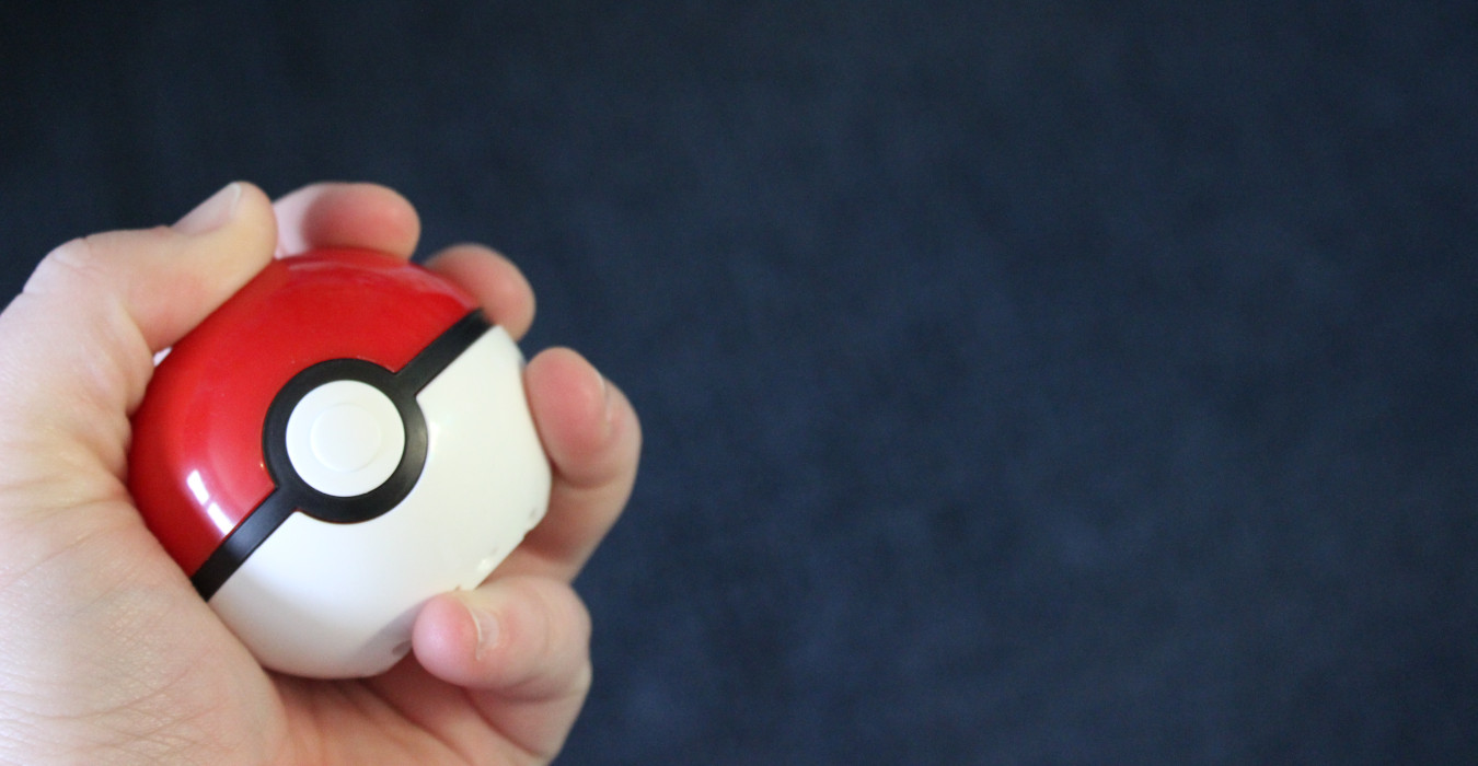 A hand holds a Pokeball toy against a dark blue background.