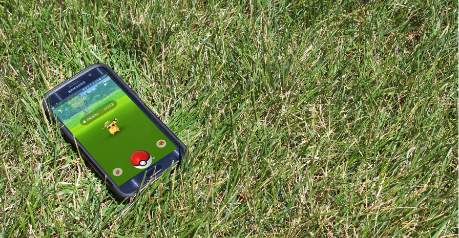 A smartphone sitting in the grass. On the screen it shows someone catching a Pikachu in Pokemon Go.