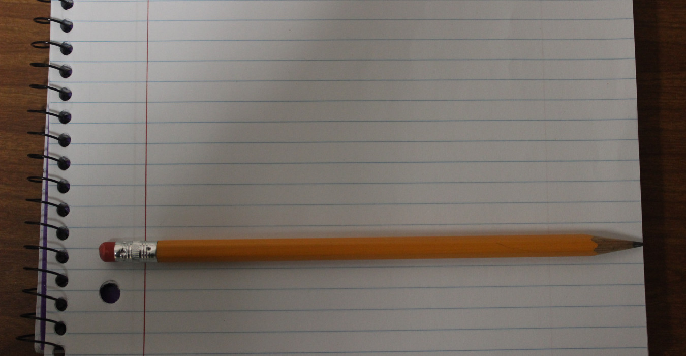 A blank notebook page sits on a desk. a #2 pencil sits on top of the page.