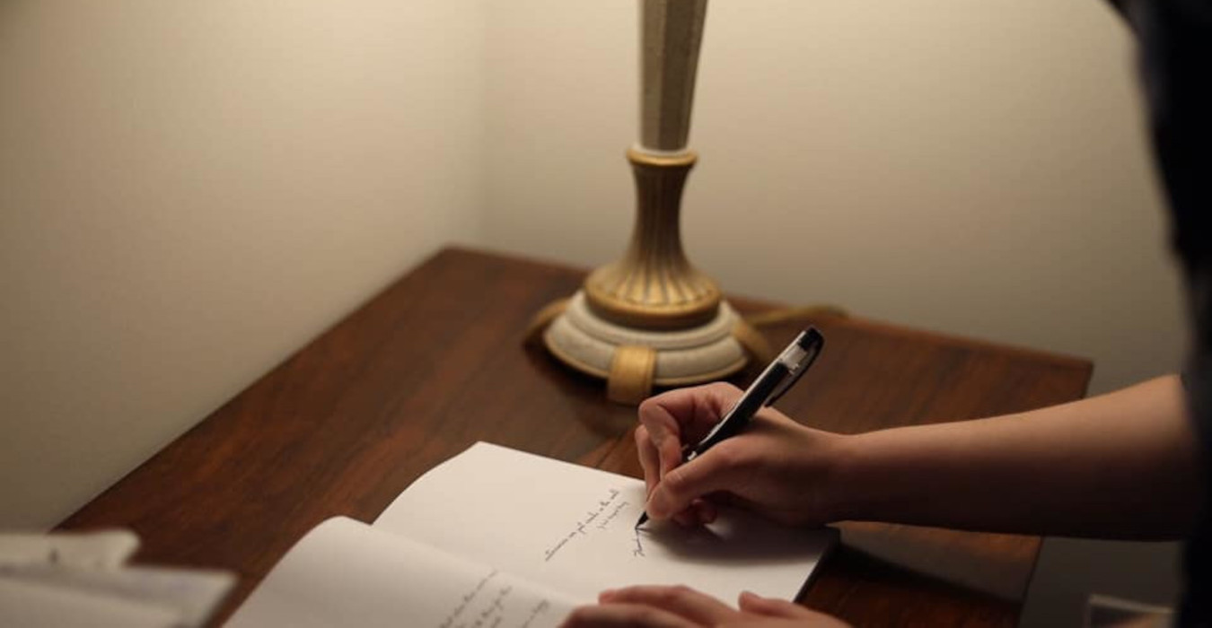 A woman stands at a desk signing a book