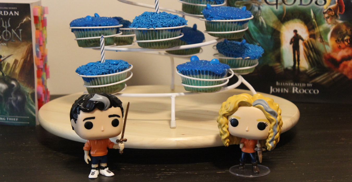 photo of figurines of Percy Jackson and Annabeth Chase standing in front of a display of blue cupcakes