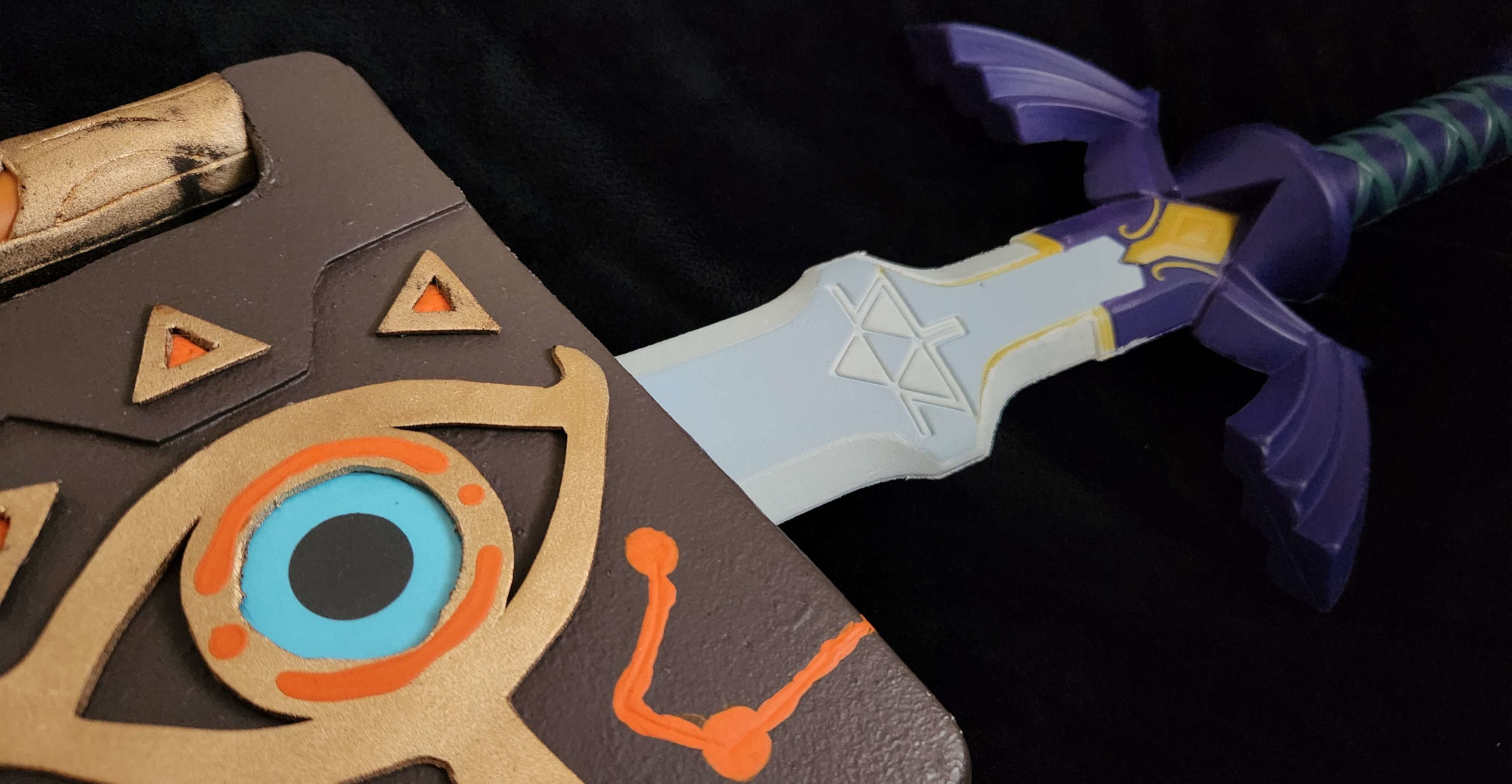 A photo showing a handmade prop of the Sheikah Slate from Breath of the Wild, as well as a foam prop of the Master Sword from the Legend of Zelda franchise.