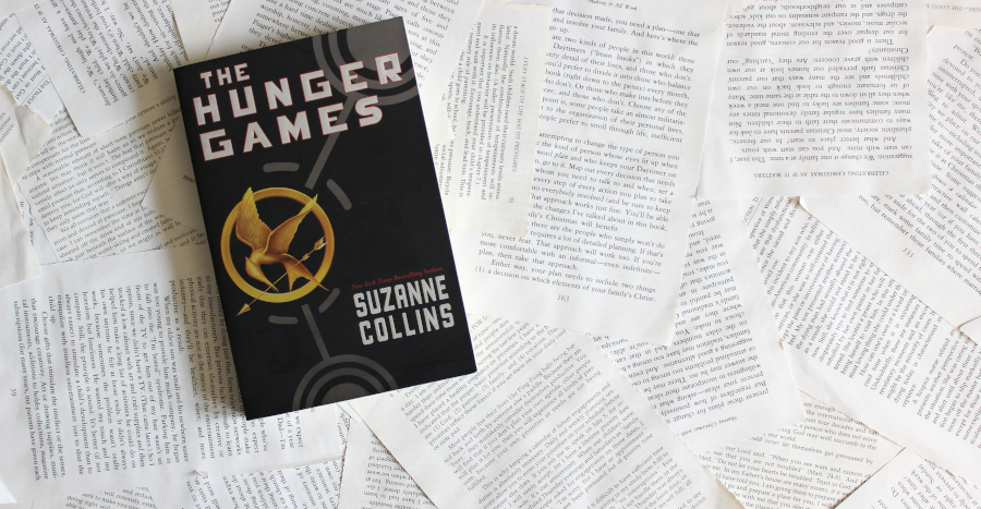 A copy of The Hunger Games sits against a background of scattered book pages.