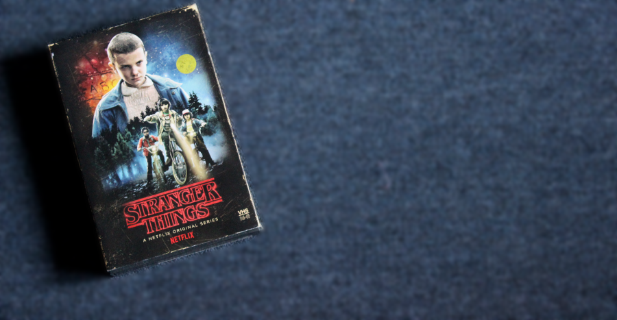 The Stranger Things Season 1 DVD/Blu-Ray collection against a dark blue background. The box is decorated to look like an old VHS tape